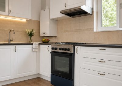 Bucatarie alba clasica in L cu blat negru, aragaz retro bleumarin, hota inox si parchet de lemn