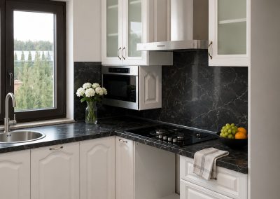 Bucatarie alba in L cu fronturi clasice, blat negru marmorat si cuptor cu microunde incorporat in coloana