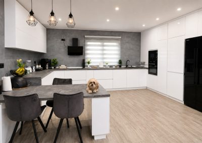 Bucătărie modernă albă în L, cu peninsulă și coloane de depozitare până în tavan, pe fundal de perete gri decorativ