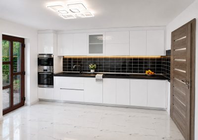 Bucatarie alba lucioasa liniara lunga cu coloana de cuptoare incorporate, blat negru si gresie imitatie marmura
