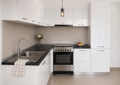 Bucatarie mica in L alb lucios, cu blat negru, aragaz inox si coloana pentru frigider
