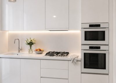 Bucatarie alba mica moderna cu blat alb, coloana cu cuptor si microunde inox si plita pe gaz