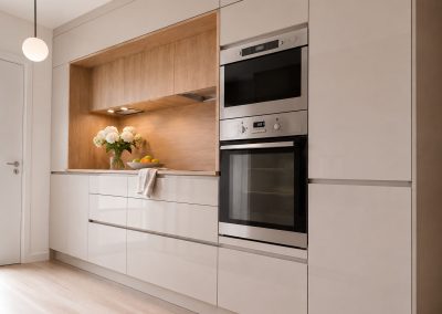 Bucatarie liniara crem lucioasa cu nisa placata in lemn, coloana cu cuptor si cuptor cu microunde inox