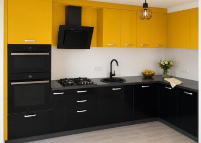 Bucatarie in L cu corpuri superioare galben mustar si corpuri inferioare negru lucios, blat negru si cuptor dublu