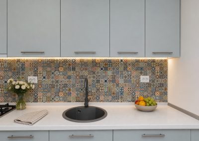 Bucatarie gri albastrui cu blat alb, faianta patchwork colorata si chiuveta rotunda neagra din compozit