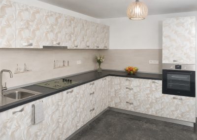 Bucatarie in L cu fronturi decorate cu model abstract crem si blat gri antracit, cuptor incorporat in coloana