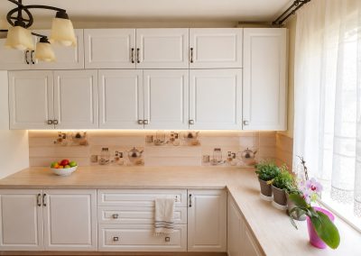 Bucatarie ivoriu clasica in U cu fronturi cu rama, blat de lemn deschis, faianta cu decor de ceainice si candelabru