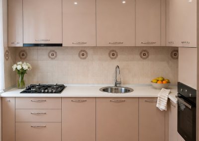 Bucatarie mica in U cu fronturi roz pudra, faianta alba cu decor floral si blat crem