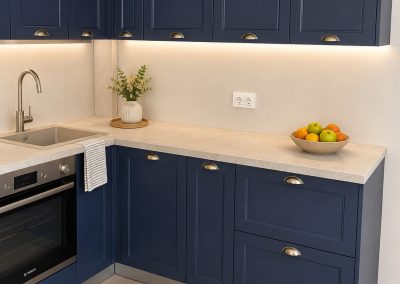 Bucătărie în L bleumarin cu fronturi înrămate tip shaker, mânere scoică din alamă, blat bej și cuptor inox