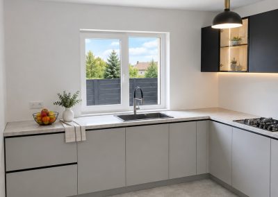 Bucătărie în L minimalistă cu corpuri jos gri deschis fără mânere, blat imitație beton și corp suspendat negru cu vitrină iluminată LED