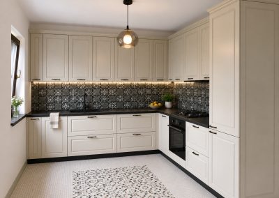 Bucătărie în L ivoire cu fronturi înrămate, mânere negre, blat negru și faianță decorativă tip azulejos